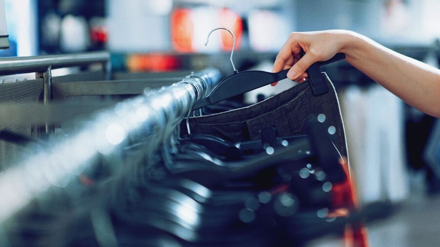 Person browsing clothes on hangers in a retail store.