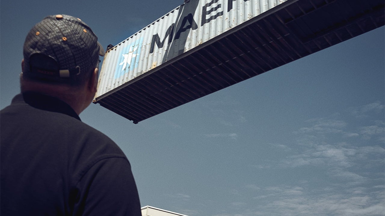 A male watching Maersk container being moved with a crane.