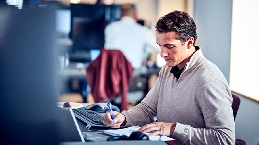 Man writing notes at his desk in a modern office environment.
