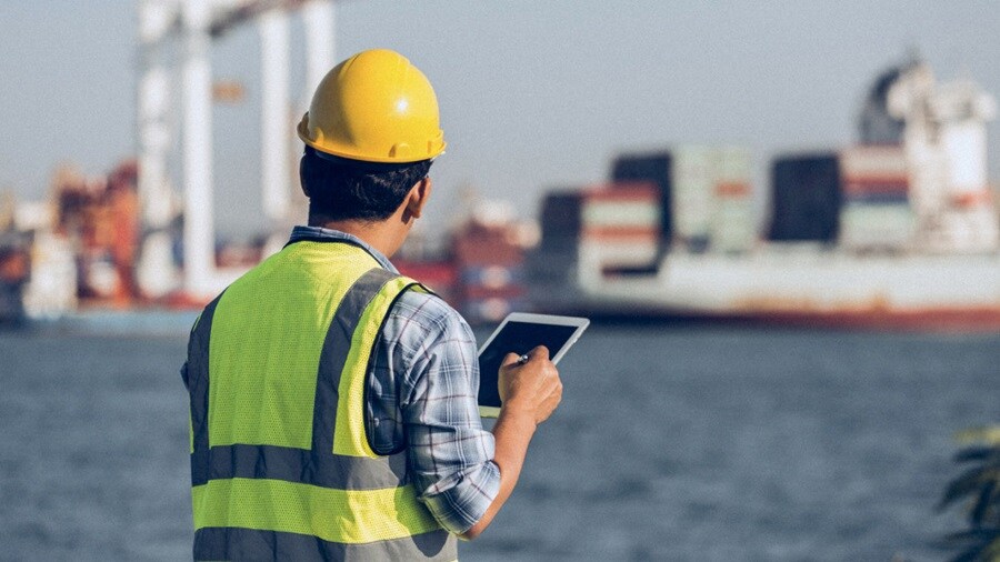 A construction worker in a hard hat and safety vest is using a tablet computer for project management.