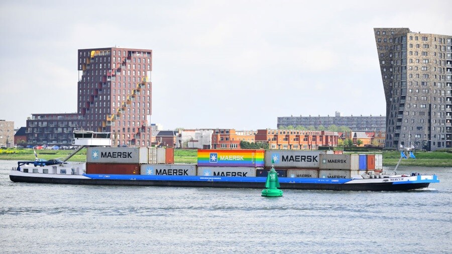 Maersk barge transporting containers through an urban waterway.