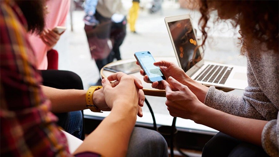 People collaborating while using a smartphone and laptop at a café.