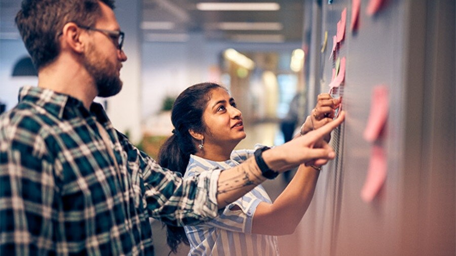 Two colleagues are collaborating by placing and discussing sticky notes on a wall.