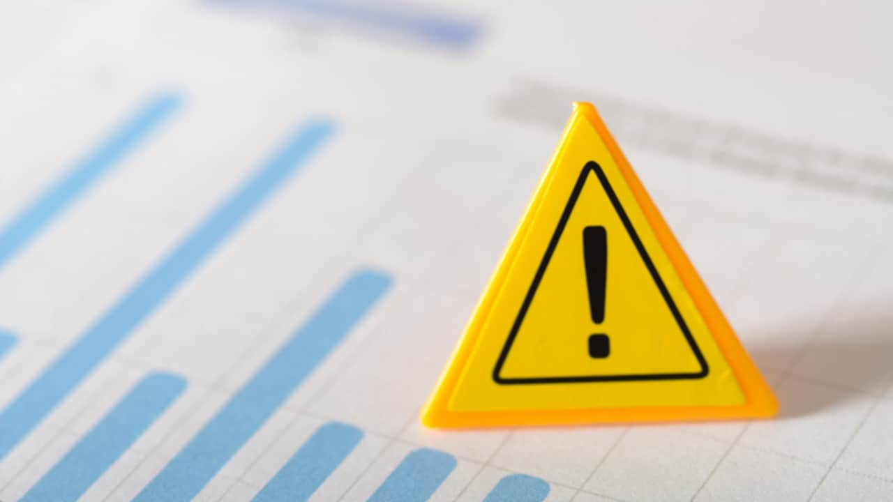 Yellow warning triangle sign placed on financial chart indicating supply chain risk signals