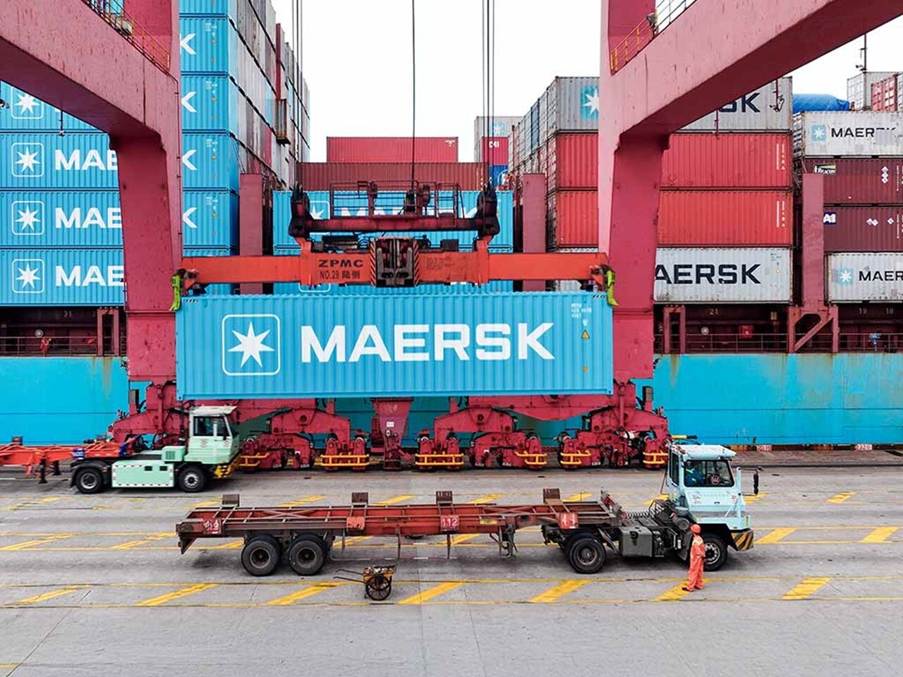 在繁忙的港口码头，龙门吊正在吊装东升国际集装箱，下方有卡车